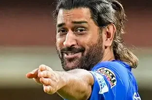 ধোনি একটি প্রাচীন মন্দিরে ভক্তিভরে দাঁড়িয়ে আছেন, পাশে পুরোহিত ও সাধারণ ভক্তরা; মুখে শান্ত, নম্র অভিব্যক্তি।
